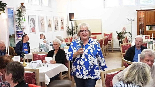 Frau mit Mikrofon im Raum mit vielen Leuten.