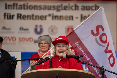 Frau spricht auf einer Bühne, im Hintergrund eine Fahne mit SoVD-Logo. 