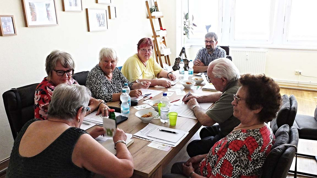 Acht Personen sitzen an einem Tisch und reden miteinander.