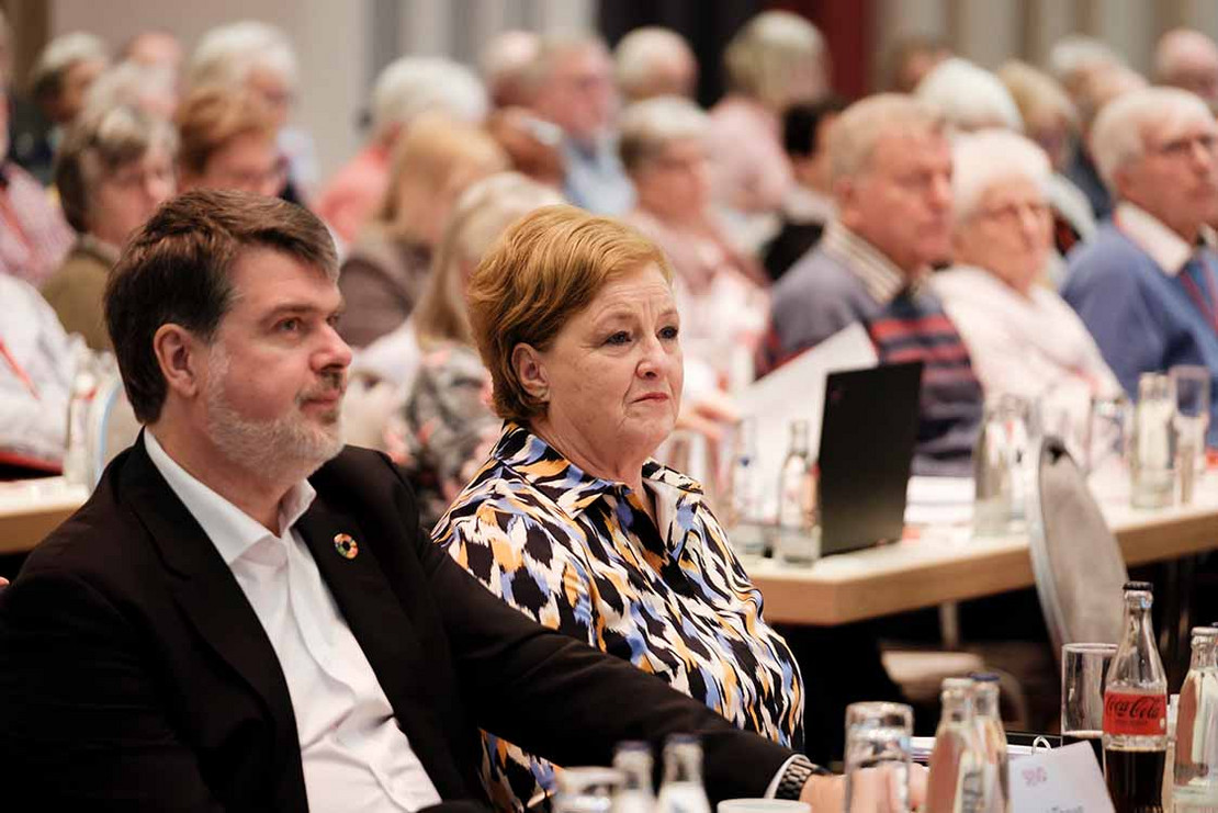 Mann und Frau verfolgen eine Rede. 