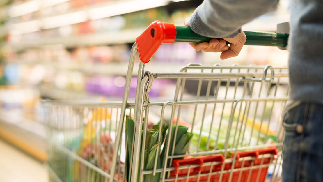 Mensch schiebt einen Einkaufswagen durch den einen Supermarkt. 