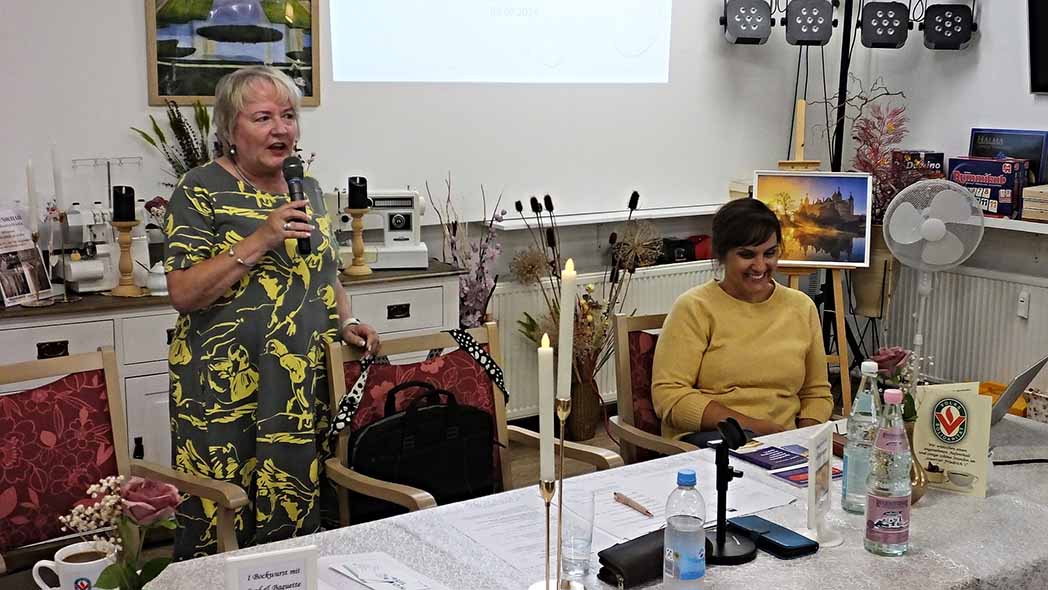 Zwei Frauen am Tisch, eine spricht in ein Mikrofon