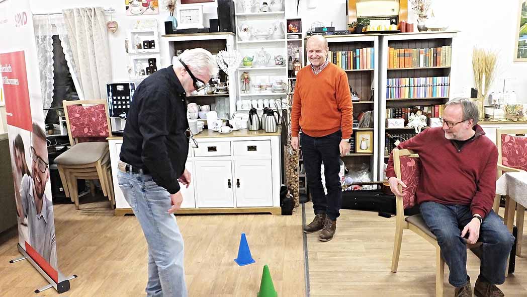 Mann mit Spezialbrille löst vor zwei Zuschauern eine Aufgabe.